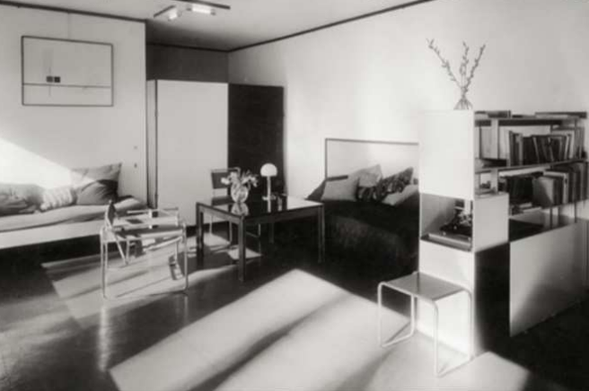 Schwarzweißfoto eines modernen Wohn-/Schlafraums mit Betten, Tisch, Stühlen und Regalen.
